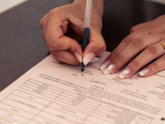 A person signing a document with a black pen on a dark table