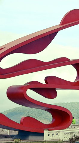 a large red sculpture sitting on top of a lush green field